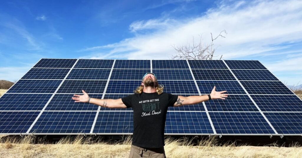Ground-mounted solar array installed in front of and beside a tiny off-grid house with rooftop solar panels in a rural setting